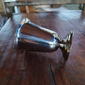May include: A silver metal goblet with a rounded base and a smooth, reflective surface.