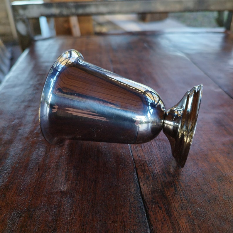 May include: A silver metal goblet with a rounded base and a smooth, reflective surface.