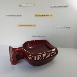 May include: A red ceramic ashtray shaped like a Grand Marnier liquor bottle with the words "Grand Marnier" in gold lettering.