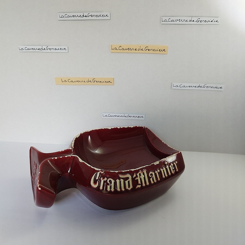 May include: A red ceramic ashtray shaped like a Grand Marnier liquor bottle with the words "Grand Marnier" in gold lettering.