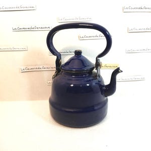 Peut inclure: Une théière en émail bleu avec un couvercle et une poignée. La théière a un bec verseur sur le côté et une petite chaîne attachée à la poignée.