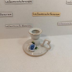 May include: White porcelain candle holder with a blue and green floral design. The holder has a small handle and a gold trim.