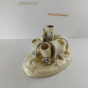 May include: A white ceramic pen holder with a floral design. The holder has four pen slots and a central slot for a larger item. The holder is decorated with silver accents and has a base that resembles a flower.