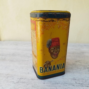 Peut inclure: Boîte Banania jaune vintage avec un visage noir souriant portant un fez rouge. La boîte de forme rectangulaire a un bord bleu et porte le nom de la marque "Banania". Il s'agit probablement d'un contenant pour un produit de petit-déjeuner.