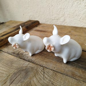 May include: A set of two white ceramic pig salt and pepper shakers with pink flower accents.