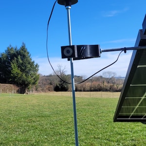 Peut inclure: Un anémomètre noir à trois coupelles monté sur un poteau argenté. L'anémomètre est relié à un panneau solaire par un fil noir.