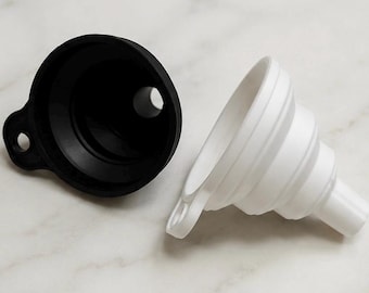 以下が含まれることがあります： 黒と白の折りたたみ式じょうごセット。黒いじょうごは広い開口部と小さなループが付いています。白いじょうごは折りたたまれており、細い注ぎ口が付いています。このセットは、保管と使用が簡単になるように設計されています。