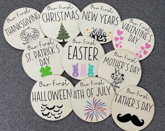 Könnte beinhalten: Satz von 10 runden Holzschildern mit schwarzem Text und Illustrationen. Jedes Schild zeigt einen anderen Feiertag oder Anlass, wie "Unser erstes Thanksgiving", "Unser erstes Weihnachten", "Unser erstes Neujahr", "Unser erster Valentinstag", "Unser erster St. Patrick's Day", "Unser erstes Ostern", "Unser erster Muttertag", "Unser erstes Halloween", "Unser erster 4. Juli" und "Unser erster Vatertag".