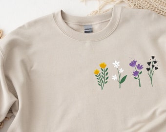 Peut inclure: Un sweat-shirt beige avec un motif floral composé de fleurs jaunes, blanches, violettes et noires. Les fleurs sont disposées en rangée sur la poitrine du sweat-shirt.