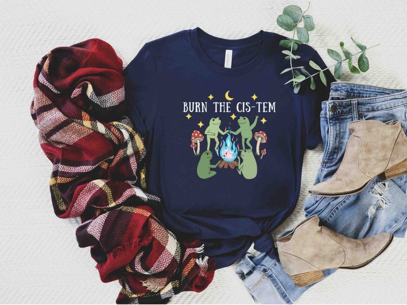 Puede incluir: Una camiseta azul marino con un gr&aacute;fico de dos ranas alrededor de una fogata con el texto "BURN THE CIS-TEM" encima.