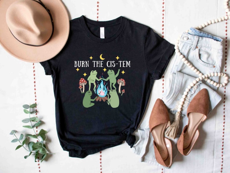 Puede incluir: Camiseta negra con un gr&aacute;fico de tres ranas verdes alrededor de una fogata con el texto "BURN THE CIS-TEM" en blanco.