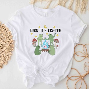 Puede incluir: Camiseta blanca con un gr&aacute;fico de cuatro ranas alrededor de una fogata con el texto "BURN THE CIS-TEM" encima.