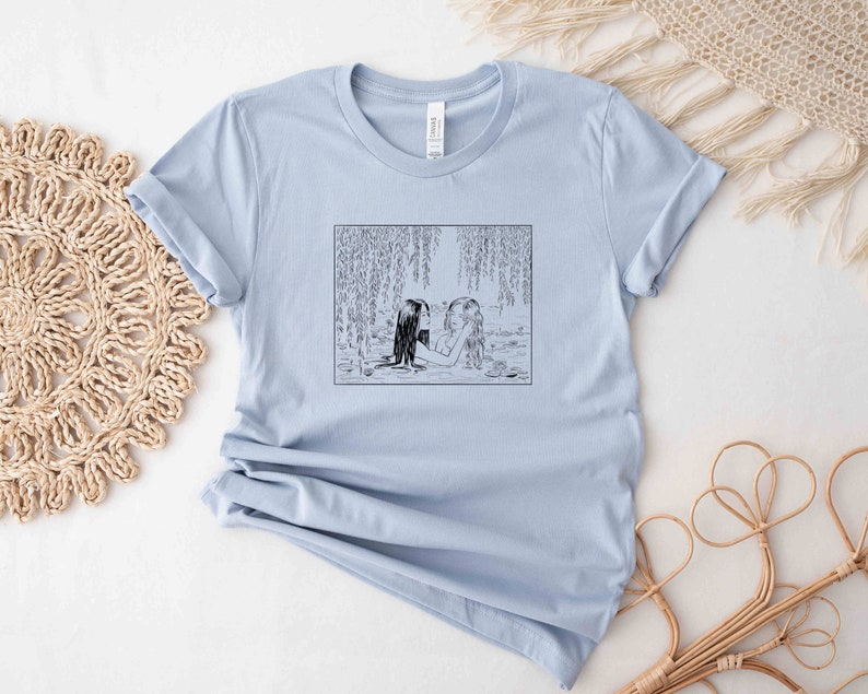May include: Light blue t-shirt with a black and white illustration of two women in a river with willow trees.