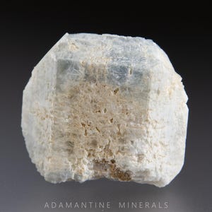 May include: A light blue and white mineral specimen with a crystalline structure. The stone has a rough, textured surface and a slightly translucent appearance. The mineral is a light, neutral color, with a subtle sheen. The overall shape is irregular, with a few defined facets.