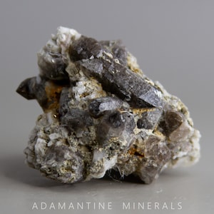 May include: A cluster of smoky quartz crystals with a rough, gray matrix. The crystals are translucent and have a smoky brown color.