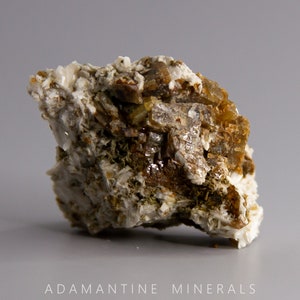 May include: A cluster of brown and white crystals on a matrix. The crystals are translucent and have a glassy luster. The matrix is a light gray color.