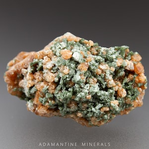 May include: A cluster of green and orange crystals. The crystals are small and have a rough texture. The cluster is about 2 inches in diameter.