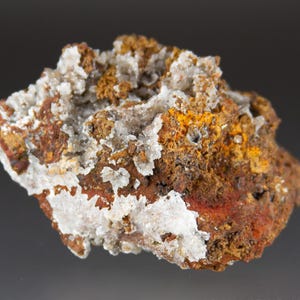 May include: A close-up of a mineral specimen with a rough, textured surface. The rock features a mix of colors, including rusty brown, orange, and white crystalline formations. The overall appearance suggests a natural, geological sample.