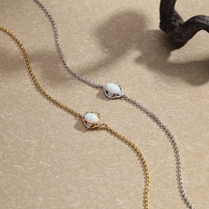 Peut inclure: Deux bracelets délicats, l'un doré et l'autre argenté, chacun orné d'une pierre centrale ovale blanche entourée d'un halo de petites pierres. Les bracelets sont présentés sur une surface de ton neutre.