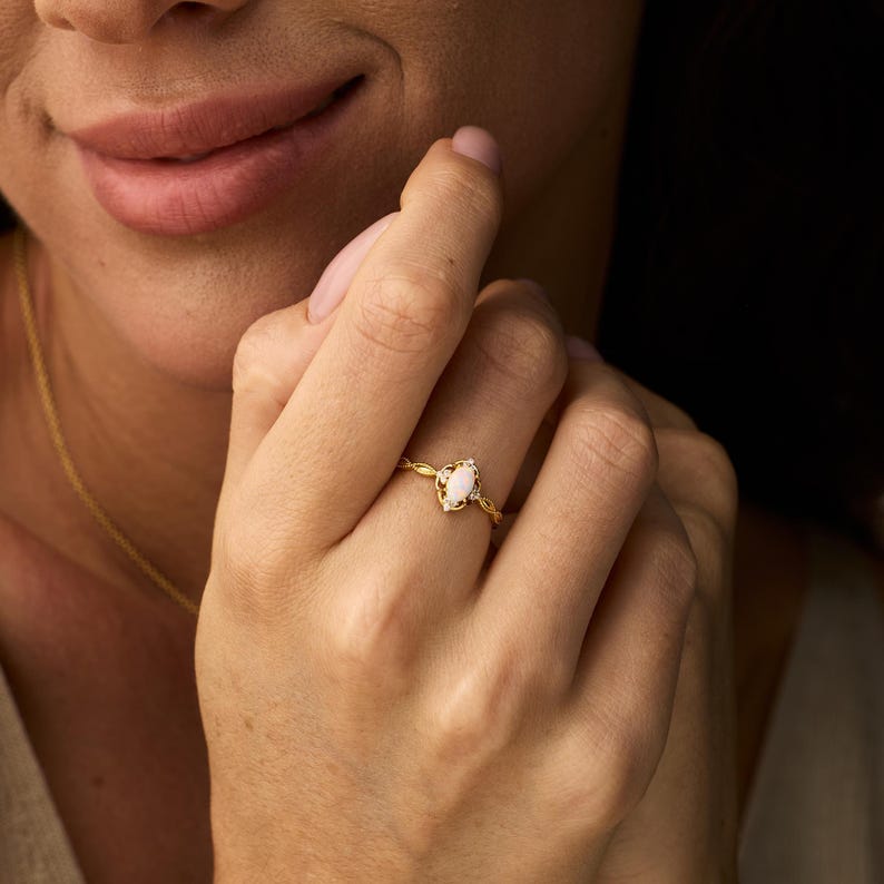 May include: A gold ring with a pear-shaped, light-colored gemstone. The ring has a delicate, twisted band and is worn on a person's finger. The ring is a piece of jewelry.