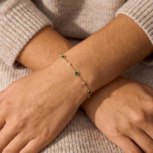 Puede incluir: Una delicada pulsera de cadena dorada que presenta una alternancia de piedras preciosas redondas de color verde y peque&ntilde;as piedras blancas transparentes engastadas en estilo bisel. La pulsera se lleva en la mu&ntilde;eca con eslabones.