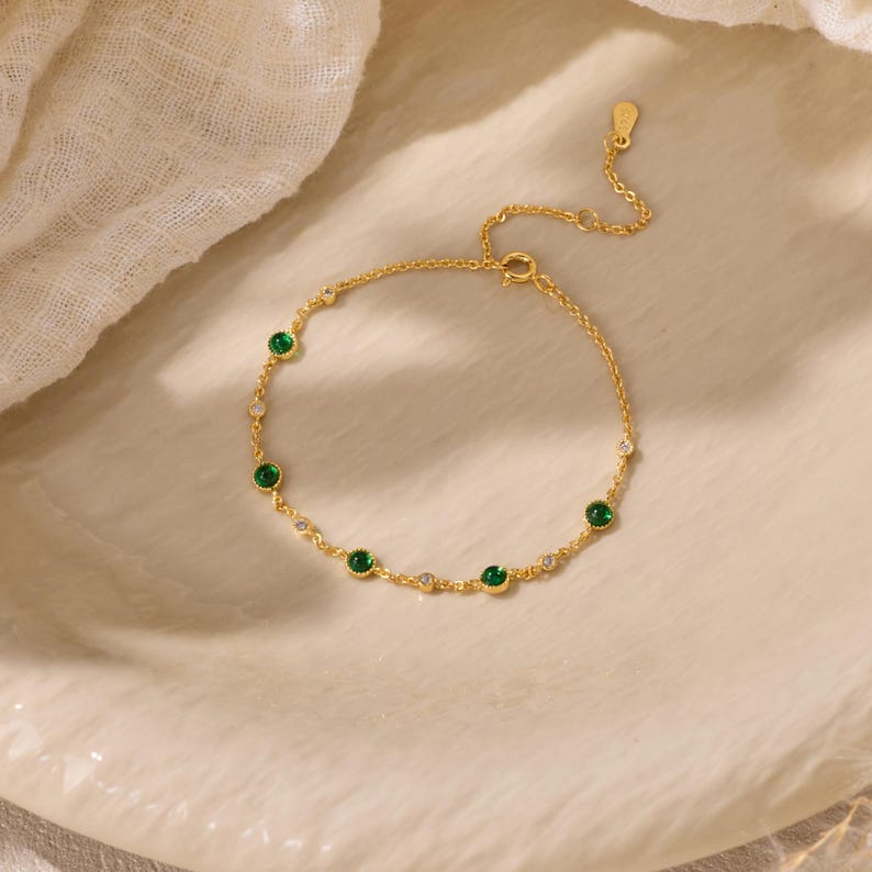 Puede incluir: Una delicada pulsera de cadena dorada con piedras redondas alternas, verdes y transparentes, engastadas en biseles dorados. La pulsera incluye una fina extensi&oacute;n de cadena con una peque&ntilde;a etiqueta dorada en el extremo.