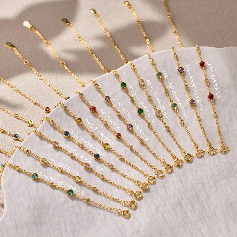 Puede incluir: Una colecci&oacute;n de pulseras de cadena en tono dorado, cada una con una piedra preciosa engastada. Las pulseras est&aacute;n etiquetadas con los nombres de los meses y las piedras correspondientes: Jan-Garnet, Feb-Amethyst, Mar-Aquamarine, Apr-Diamond, May-Emerald, Jun-Alexandrite, Jul-Ruby, Aug-Peridot, Sept-Sapphire, Oct-Tourmaline, Nov-Citrine y Dec-Blue Topaz.