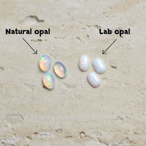 May include: Image showing two groups of oval-shaped opals. The text "Natural opal" points to a group of three opals with iridescent colors. The text "Lab opal" points to a group of three white opals with a subtle sparkle.