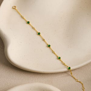 Puede incluir: Una delicada pulsera de cadena dorada que presenta una serie de piedras redondas de color verde vibrante espaciadas uniformemente, alternadas con piedras m&aacute;s peque&ntilde;as, claras y brillantes. La pulsera tiene una cadena fina y un cierre.