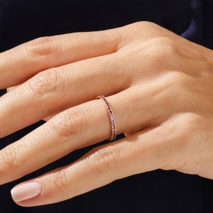 Peut inclure: Une délicate bague éternelle avec une rangée de petites pierres précieuses rouges serties dans une fine bande d'or.