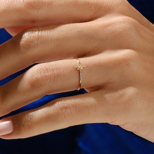 Puede incluir: Un delicado anillo de oro con un pequeño diamante en forma de estrella en el centro.
