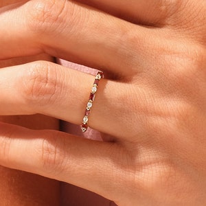 May include: A delicate gold band ring with alternating red gemstones and small diamonds.