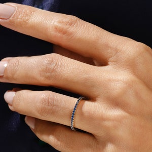May include: A delicate gold band ring with a row of small, dark blue sapphires.