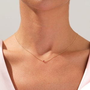 May include: A delicate gold chain necklace with a small red gemstone pendant.