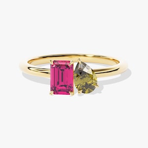 May include: A gold ring with two gemstones. The larger gemstone is a pink emerald cut stone. The smaller gemstone is a pear-shaped green stone.