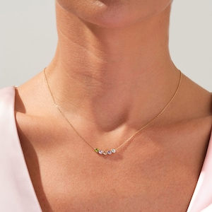 May include: A gold chain necklace with five small gemstones in a rainbow of colors. The necklace is on a model's neck.