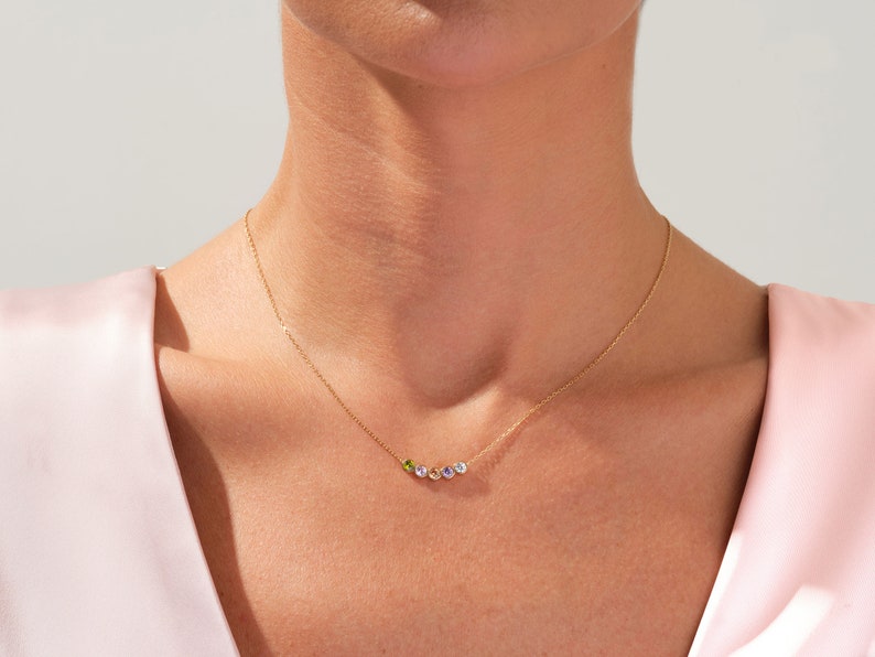 May include: A gold chain necklace with five small gemstones in a rainbow of colors. The necklace is on a model's neck.