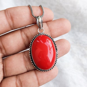 May include: A silver pendant necklace with a large, oval-shaped red gemstone set in a silver bezel. The pendant has a detailed, rope-like border.