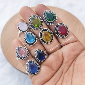 Puede incluir: Un conjunto de diez anillos de plata con acentos de piedras preciosas de colores. Cada anillo presenta una piedra en forma de lágrima en una variedad de colores, incluyendo rosa, azul, verde, amarillo y rojo. Los anillos están todos engastados en una banda de plata con un diseño decorativo.