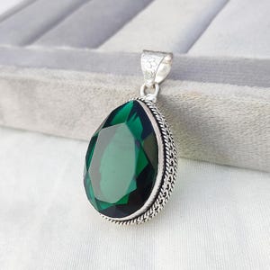 Pode incluir: Um pingente de prata com uma grande gema verde facetada em forma de lágrima.