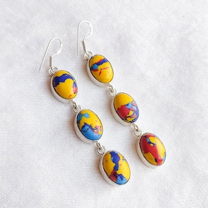 May include: A pair of long silver dangle earrings with three oval-shaped stones. The stones are a mix of yellow, red, and blue.