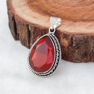May include: A red gemstone pendant with a silver setting. The pendant is shaped like a teardrop and has a detailed rope-like border.