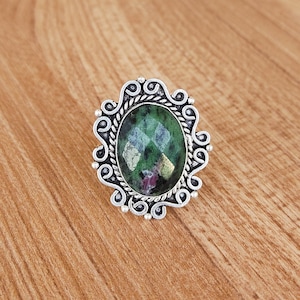 May include: A silver ring with an oval-shaped green and pink gemstone set in a decorative filigree design.