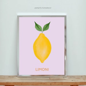 May include: A framed print featuring a watercolor illustration of a yellow lemon with green leaves against a light pink background. The word "LIMONI" is printed in orange at the bottom. The frame is silver, and the artwork is displayed on a wooden surface.