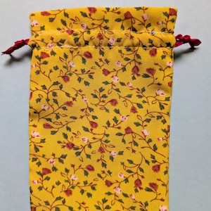 May include: A yellow drawstring bag with a floral pattern of red and white flowers and green leaves. The bag has a red drawstring closure.