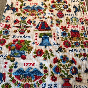 May include: A vintage fabric with a repeating patriotic design. The off-white background is covered with illustrations of the Liberty Bell, eagles, sailboats, and floral arrangements in red, blue, and green. The word "Freedom" and the number "1776" are also visible.
