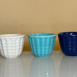 May include: Three small ceramic bowls arranged in a row, featuring a white bowl, a turquoise bowl, and a dark blue bowl. Each bowl has a consistent textured pattern of horizontal wavy lines embossed around the exterior surface.