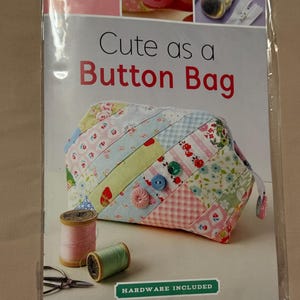 May include: A sewing kit titled "Cute as a Button Bag" featuring a patchwork bag with floral and pastel patterns. The kit includes buttons, wire, and a zipper. Two spools of thread and scissors are also visible.