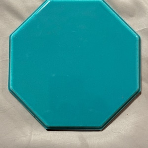 May include: A turquoise octagonal tile with a glossy finish. The tile has a smooth surface and a beveled edge. This decorative tile can be used for various home decor projects.