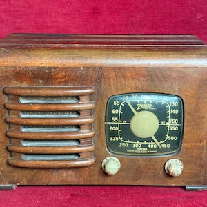 May include: A vintage Zenith tabletop radio with a dark brown wooden cabinet, featuring a horizontal slatted speaker grille on the left and a black tuning dial with white numbers and a central cream-colored knob on the right side.